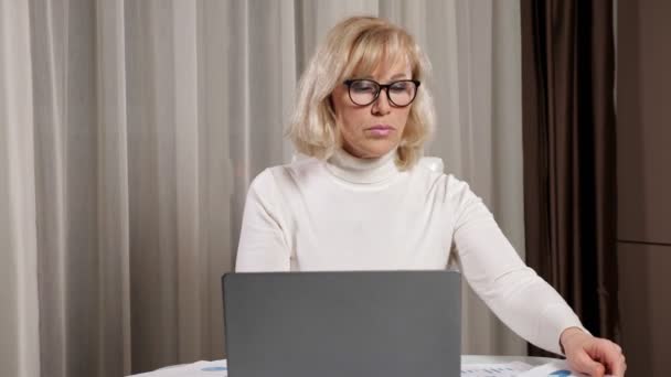 Mujer madura en gafas mira a través de los papeles de la factura de servicios públicos — Vídeos de Stock