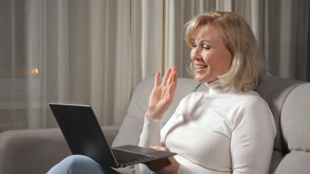 Kadın bilgisayar kullanarak video aracılığıyla konuşuyor ve kanepede oturuyor. — Stok video
