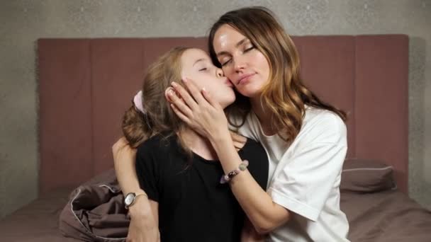 Mother and daughter kiss each other talking on bed at home 