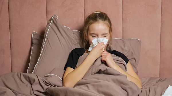 Adolescente chica tose y sopla la nariz con servilleta en el dormitorio —  Fotos de Stock