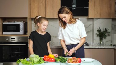 Anne, kızının mutfakta salatalık kestiğini gösteriyor.