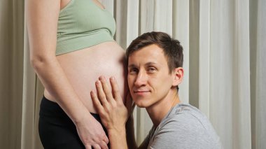 Erkek, karısının karnında doğmamış bir bebeği okşar ve dinler.