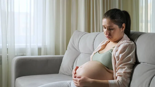 Pregnant woman sits on sofa upset from gaining weight — Stock Photo, Image