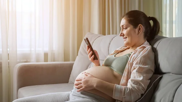 Pregnant woman reads news in internet using smartphone — Stock Photo, Image