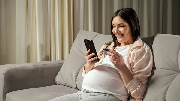 임신 한 브루넷은 휴대폰을 통해 온라인 쇼핑에 대한 비용을 지불 한다 — 스톡 사진