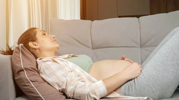 Femme enceinte se trouve sur le canapé caressant ventre nu soigneusement — Photo