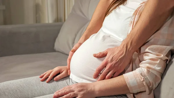Young man caresses pregnant belly of wife sitting on sofa — Stock Photo, Image
