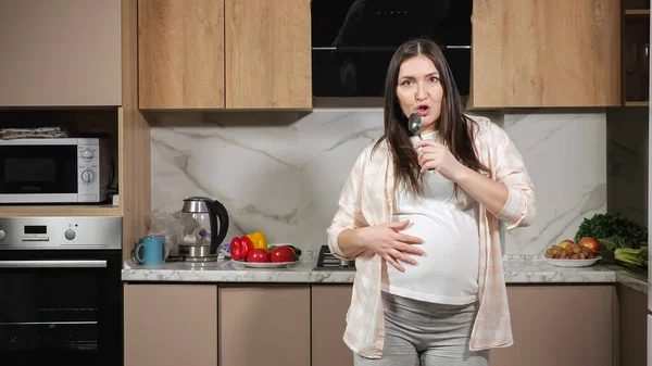 Pregnant woman sings with spoon imitating microphone dances — Stock Photo, Image