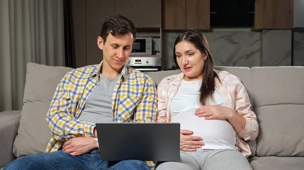 남편 과 임신부는 인터넷으로 소파에 앉아 쇼핑을 한다 — 스톡 사진
