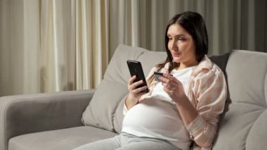 Esmer hamile kadın internet alışverişini telefonla yapıyor.