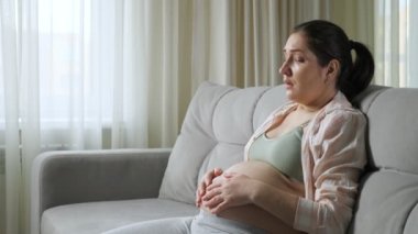 Hamile kadın kilo aldığı için üzgün bir şekilde koltukta oturuyor.