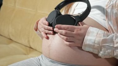 Tanımlanamayan hamile kadın kulaklıkları mideye indirir, çocuk hoş müzik dinler.
