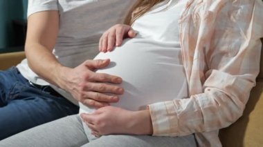 Bir çift, ailesinin geleceğini bekliyor. Koltukta oturan ebeveynler. Bir erkek, hamile kadınların karnını okşuyor.