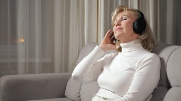 Orta yaşlı sarışın kadın kulaklıkla müzik dinliyor. — Stok video