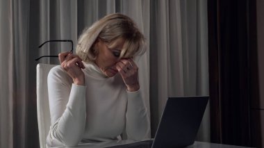 Orta yaşlı bir kadın geceleri laptopta çalışmaktan yorgun düşüyor.