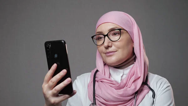 Μουσουλμάνα γιατρός χαμογελά surfing internet μέσω τηλεφώνου — Φωτογραφία Αρχείου