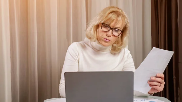 Mature woman in eyeglasses looks through utility bill papers — Stock Photo, Image