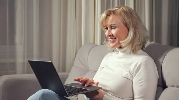Dame talks via videocall using laptop and sitting on sofa — Stock Photo, Image