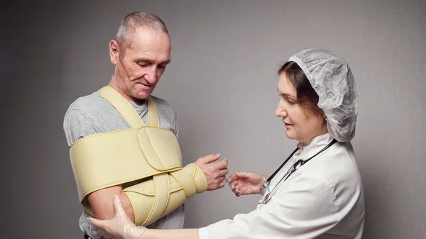 Dama ortopedista comprueba huesos de la mano de anciano con vendaje — Foto de Stock