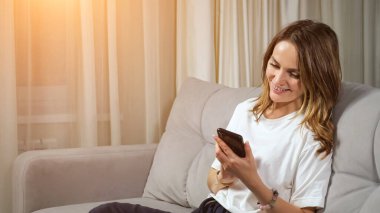 Evdeki koltukta oturan bir kadın cep telefonuna mesaj yazıyor.