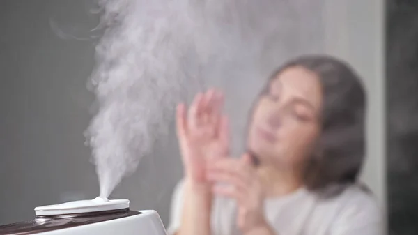 Молодая женщина наносит крем на руки, наслаждаясь увлажненным воздухом — стоковое фото