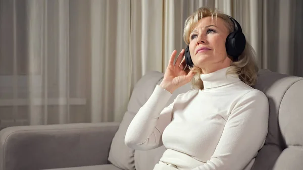 Mujer rubia de mediana edad escucha música a través de auriculares Imágenes de stock libres de derechos