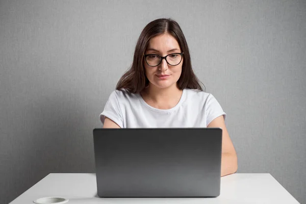 Jovem mulher com óculos senta-se em um laptop — Fotografia de Stock