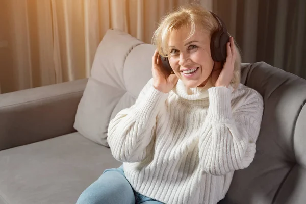 Blond kvinna i medelåldern lyssnar på musik via hörlurar Stockbild