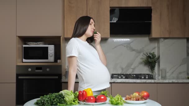 Mulher come legumes acariciando barriga grávida na cozinha — Vídeo de Stock