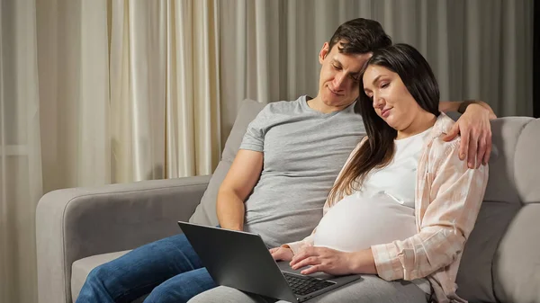 Married couple does online shopping for baby hugging on sofa — Stock Photo, Image