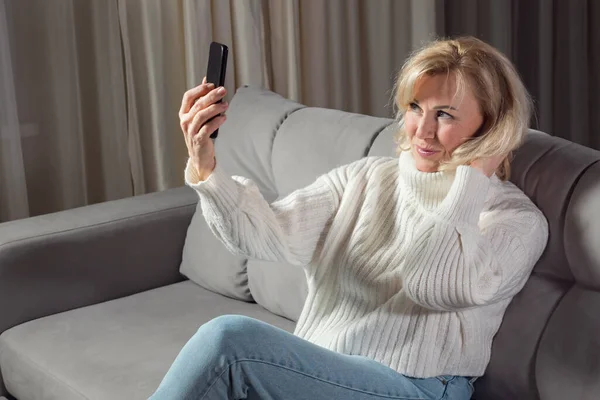 Elderly blonde woman takes selfies using cellphone — Stock Photo, Image