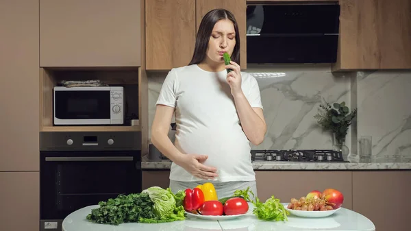 Mujer come verduras acariciando vientre embarazada en la cocina Fotos de stock libres de derechos