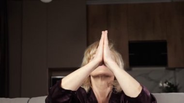Olgun sarışın kadın yoga yapıyor kanepede meditasyon yapıyor.