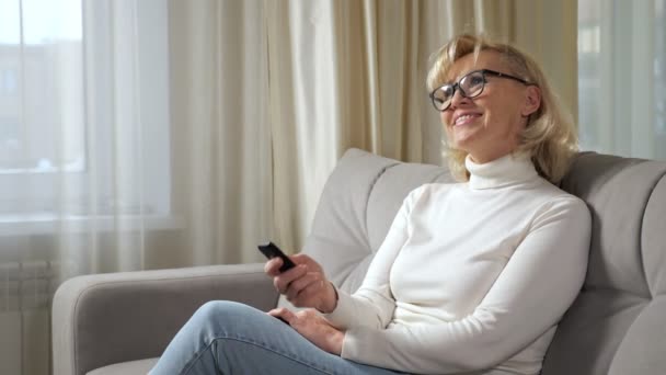 Elderly blonde woman laughs and enjoys watching TV series — Stock Video