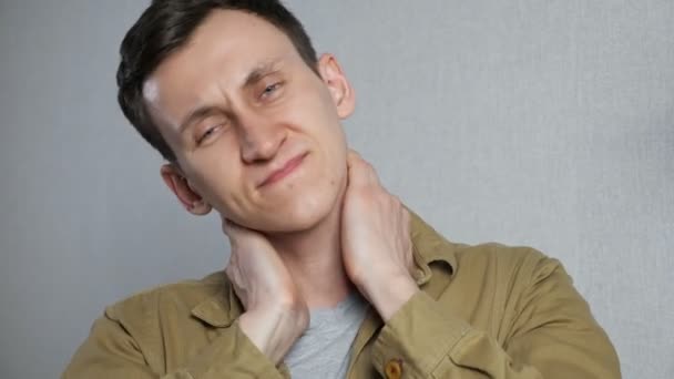 Zmęczony młody człowiek cierpiący na ból szyi stojąc na szarym tle — Wideo stockowe