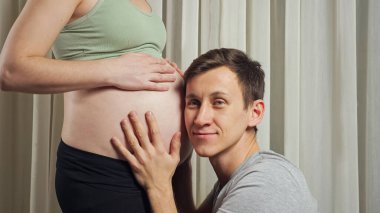 Erkek, karısının karnında doğmamış bir bebeği okşar ve dinler.