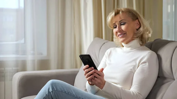 Middle aged woman scrolls through social media via phone — Stock Photo, Image