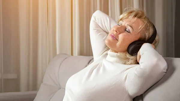 Mulher loira de meia idade ouve música via fones de ouvido — Fotografia de Stock