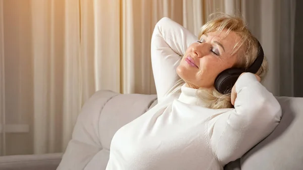 Blondine vrouw van middelbare leeftijd luistert naar muziek via de hoofdtelefoon Rechtenvrije Stockafbeeldingen