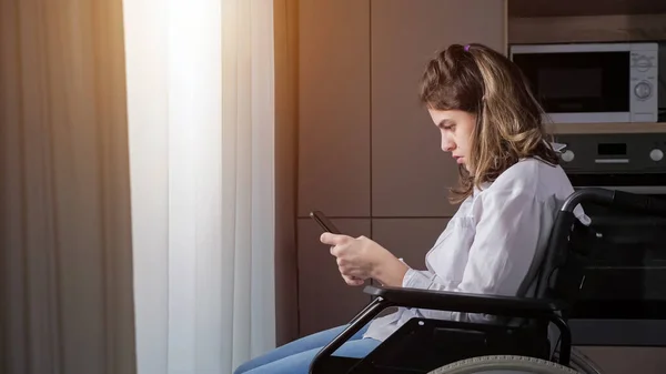 Disabled woman in wheelchair tries to use smartphone at home — Stock Photo, Image