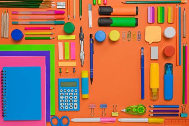 Turuncu arka planda çeşitli ofis malzemeleri var. Eğitim kavramı