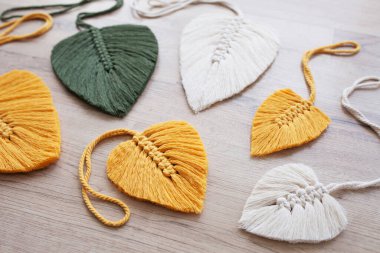 Ahşap arka planda sarı, yeşil ve doğal renklerde Macrame yaprakları. Evinizi daha samimi ve eşsiz yapmak için pamuk ip dekoru..