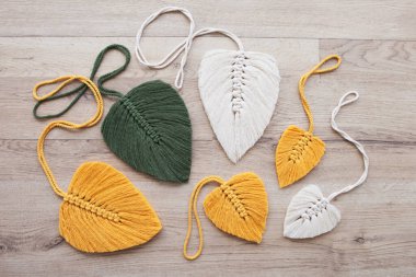 Ahşap arka planda sarı, yeşil ve doğal renklerde Macrame yaprakları. Evinizi daha samimi ve eşsiz yapmak için pamuk ip dekoru..