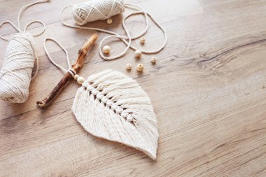 Doğal renklerde Macrame yaprağı ve ahşap bir masada uzanan iplik sargıları. Odanı daha rahat ve benzersiz yapmak için pamuk ip makrome. Kadın hobisi. El yapımı duvar asma dekoru. Boşluğu kopyala