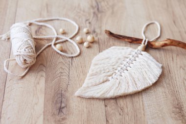 Doğal renklerde Macrame yaprağı ve ahşap bir masada uzanan iplik sargıları. Odanı daha rahat ve benzersiz yapmak için pamuk ip makrome. Kadın hobisi. El yapımı duvar asma dekoru. 
