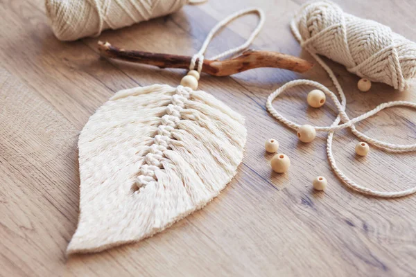 Doğal renklerde Macrame yaprağı ve ahşap bir masada uzanan iplik sargıları. Odanı daha rahat ve benzersiz yapmak için pamuk ip makrome. Kadın hobisi. El yapımı duvar asma dekoru. 