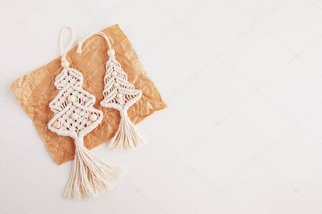 Christmas macrame decor. Christmas trees on craft paper, white background. Natural materials - cotton thread, wood beads. Eco decorations, ornaments, hand made decor. Winter and New Year holidays.