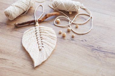 Doğal renklerde Macrame yaprağı ve ahşap bir masada uzanan iplik sargıları. Odanı daha rahat ve benzersiz yapmak için pamuk ip makrome. Kadın hobisi. El yapımı duvar asma dekoru. Boşluğu kopyala