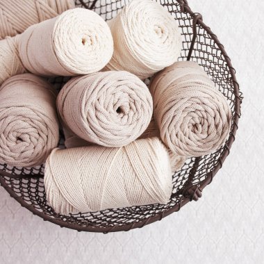 Beyaz arka planda el yapımı makrome örgü ve pamuk iplikler. Pamuk makrome kablolar ve ipler tel sepetine karşı. Makrome ve el sanatları afişleri ve reklam için iyi bir görüntü. Kapatın. Boşluğu kopyala