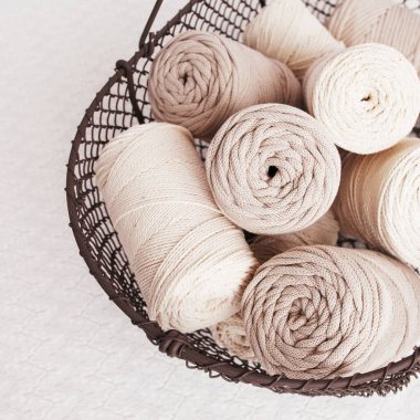 Beyaz arka planda el yapımı makrome örgü ve pamuk iplikler. Pamuk makrome kablolar ve ipler tel sepetine karşı. Makrome ve el sanatları afişleri ve reklam için iyi bir görüntü. Kapatın. Boşluğu kopyala